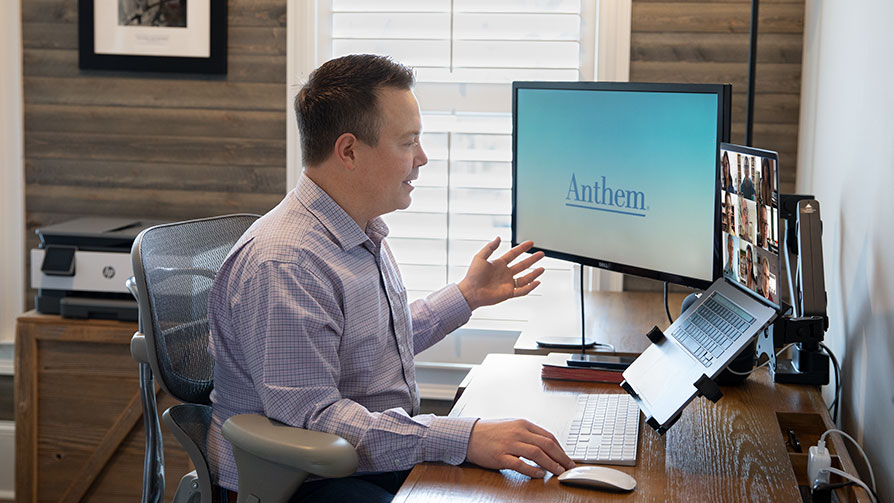 Man wearing a shirt sitting in an office talking and looking at a laptop screen with faces